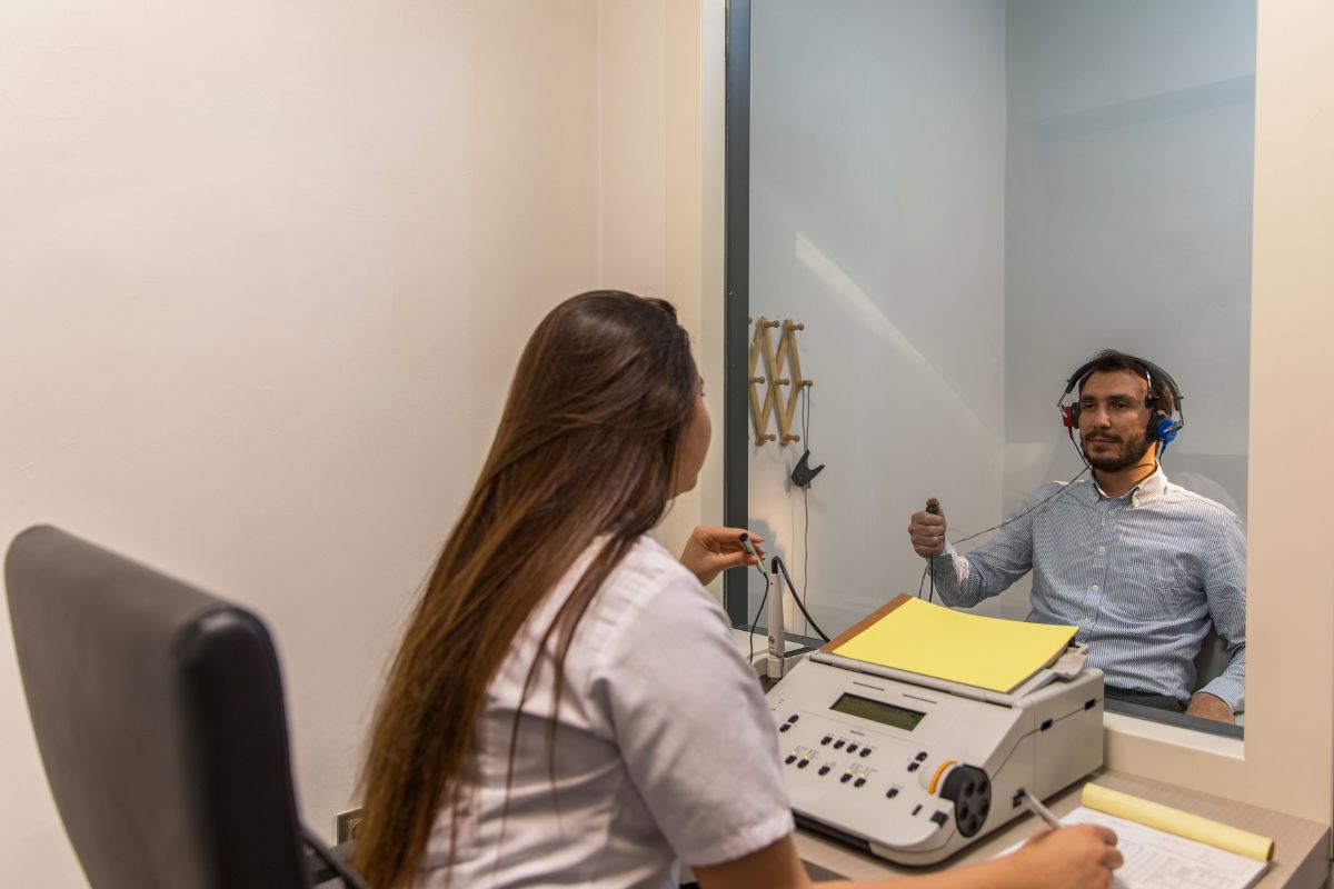 Fonoaudiólogo explicando exame de acufenometria em tela de computador para paciente sênior em consultório aconchegante, paleta azul-marinho e dourado suave, iluminação natural, fotografia realista